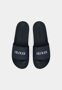 Ein Paar dunkelblaue Slide-Sandalen mit schwarzen Fußbetten, weißem "HILFIGER"-Text auf den Riemen und geprägten "TOMMY HILFIGER"-Logos auf den Fußbetten.