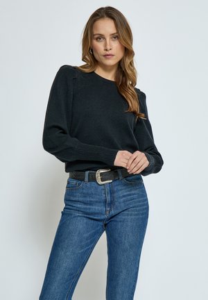 Black knitted sweater with ribbed cuffs and hem, paired with light blue denim jeans. Model wears a black belt with a silver buckle.