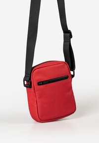 Borsa a tracolla in tessuto sintetico rosso, di forma quadrata, con una tasca con zip sulla parte anteriore e una tracolla nera regolabile per comodità.