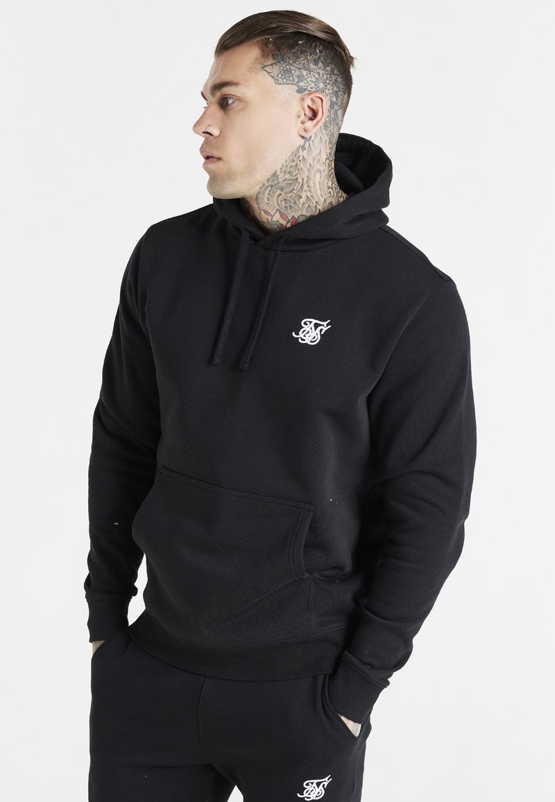 Sweatshirt à capuche noire en tissu texturé, doté d'une poche frontale et d'un petit logo blanc sur la poitrine.