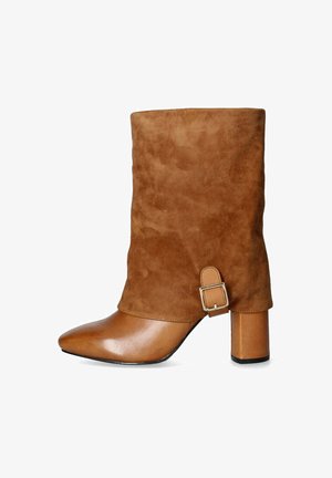 Stivaletti alla caviglia in suede marrone con punta appuntita, tacco a blocco e una cinturina con dettaglio della fibbia argentata nella parte superiore. Texture morbida in tutto il design.