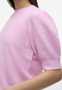 Różowy sweter z dzianiny z bufiastymi krótkimi rękawami i prążkowanymi mankietami. Tekstura wydaje się miękka i puszysta, z okrągłym dekoltem.
