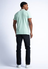 Miętowa koszulka polo z czerwonym kołnierzykiem i akcentami na rękawach, w połączeniu z czarnymi dżinsami i białymi trampkami, widok z tyłu.