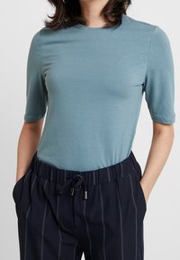 Camiseta ajustada de color azul claro con mangas cortas, hecha de un tejido suave. Combinada con pantalones marinos con rayas verticales blancas y una cintura ajustable.