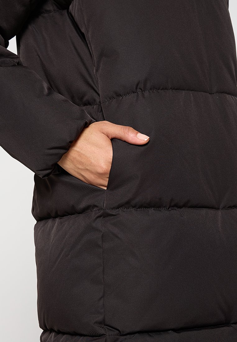 Schwarze gepolsterte Jacke mit glatter Textur, ausgestattet mit einer Seitentasche und genähten Abschnitten, die ihre Isolierung und ihr Design hervorheben.