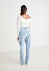 Jasnoniebieskie dżinsy z wysokim stanem o luźnym kroju, z denimu, z widocznymi tylnymi kieszeniami, zestawione z białą bluzką z długim rękawem.