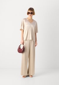 Beige satin top with short sleeves and V-neck, paired with wide-leg beige trousers. Holding a small burgundy crocodile-embossed handbag.
