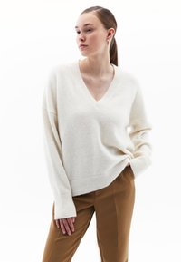Maglione crema a scollo a V realizzato in un morbido tessuto testurizzato, con maniche ampie, abbinato a pantaloni eleganti marroni.