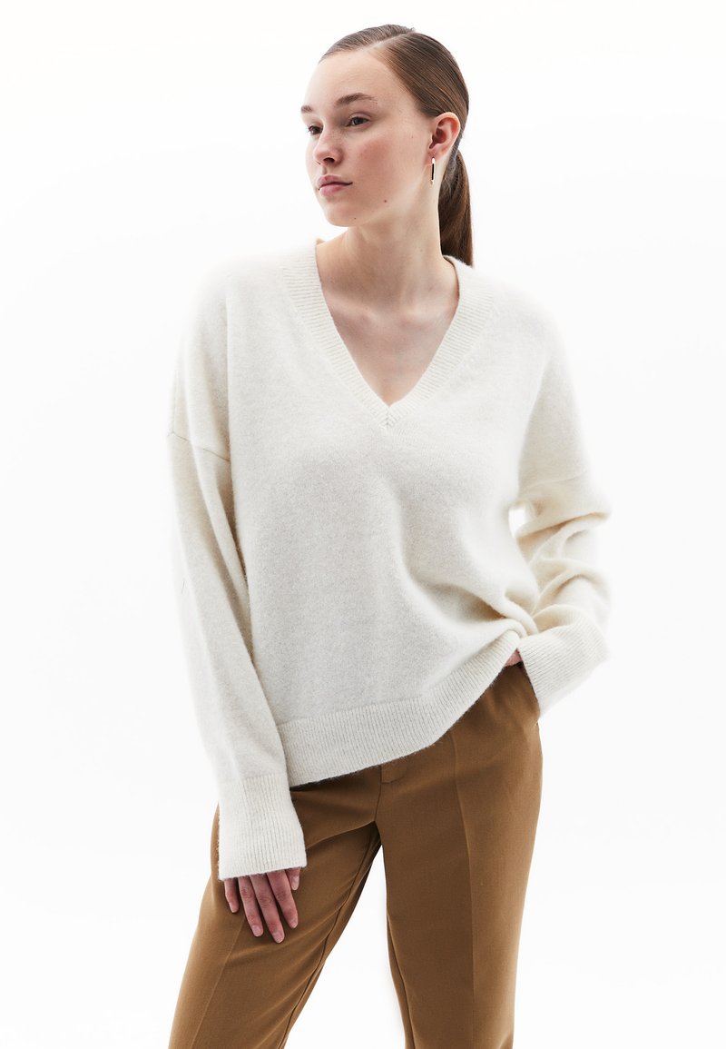 Maglione crema a scollo a V realizzato in un morbido tessuto testurizzato, con maniche ampie, abbinato a pantaloni eleganti marroni.