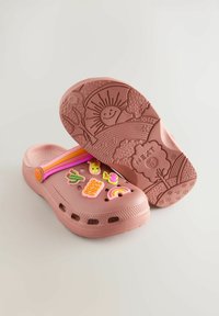 Zoccoli di gomma rosa con simpatici charm decorativi colorati, tra cui un arcobaleno, un cactus e un sole, dotati di una suola texturizzata con un motivo paesaggistico.