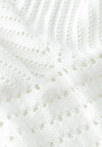 Witte gebreide deken met textuurpatronen met verhogingen en gaten, die een zachte en comfortabele uitstraling toont.