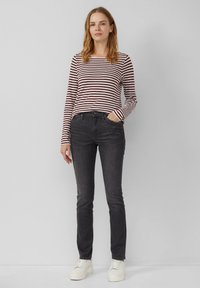 Haut à manches longues rayé rouge et blanc, associé à un jean gris foncé et des baskets blanches. Coupe slim, tissu léger, design décontracté.
