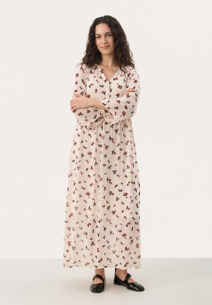 Langes, fließendes Kleid aus leichtem Stoff mit einem beigen Hintergrund und verstreuten dunklen Blumenmustern. Es hat einen V-Ausschnitt und lange Ärmel.