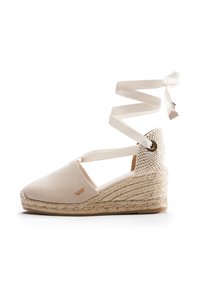 Espadrillas in tela beige con zeppa in juta intrecciata, dotate di una cinghietta incrociata alla caviglia e di un accento in tessuto testurizzato sul tallone. Dettaglio logo sottile visibile.