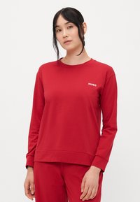 Rød longsleeve hettegenser laget av myk stoff, med rund hals og en hvit "HUGO" logo på venstre side. Enkelt design, uten mønstre.