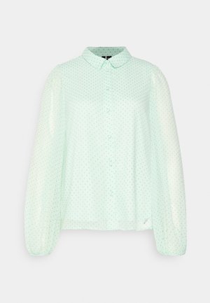 Blusa verde menta clara com botões na frente, colarinho e mangas bufantes. Apresenta pequenas bolinhas teal em tecido transparente, criando uma textura delicada.