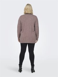 Dugi rukav, oversized pulover u mauve pletenom materijalu, sa rebrastim rubom i leđima, uparen s crnim uskim hlačama i čizmama do gležnja.