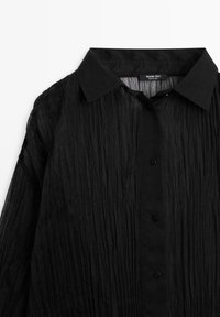 Camicia nera con tessuto strutturato e stropicciato. Presenta un colletto standard e una chiusura frontale con bottoni neri, con una vestibilità comoda.