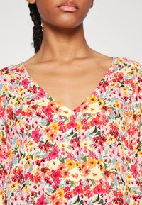 Blusa floral com decote em V, mangas curtas e um padrão multicolorido com tons de rosa, amarelo e verde sobre um fundo claro.