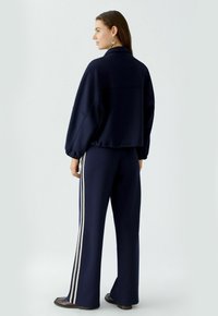 Marineblauw trainingspak met een cropped sweatshirt en wijde broekspijpen. Bevat contrasterende witte zijkanten en een zachte, getextureerde stof.