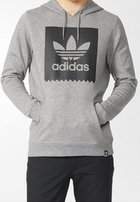 Felpa grigia in cotone con logo Adidas nero, tasca a marsupio anteriore, cordini e polsini e orlo a costine.