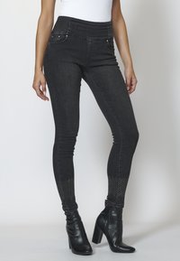 Svart denim skinny jeans med hög midja, framfickor och nitar vid fållarna. Matchas med svarta klackade ankelboots.