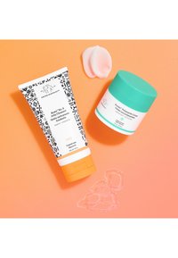 Drunk Elephant Beste No. 9 jelly cleanser in a patterned tube with orange cap and Protini Polypeptide cream in a teal-lidded jar on orange background.