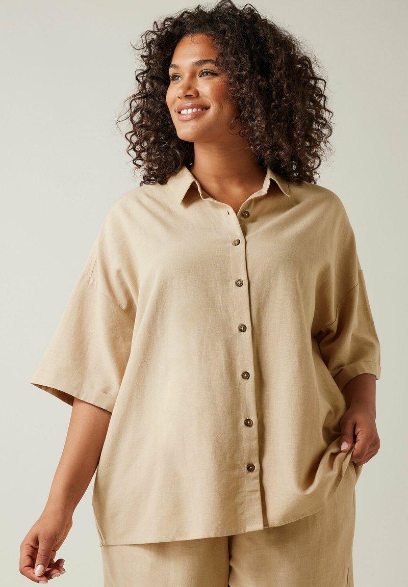 Camicia beige con bottoni realizzata in tessuto leggero, con una vestibilità comoda, maniche corte e un orlo leggermente curvato.