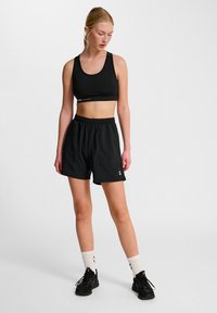 Svart sportbh med bred hängslen och ärmlös design, ihop med svarta shorts med elastisk midja och sidofickor. Svarta sneakers.
