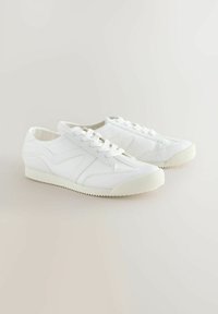 Hvide sneakers med tekstureret læder, letvægtsdesign, rund tå og en rillet gummisål. Snørebånd og diskrete side mønstre er inkluderet.