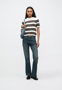 Gestreifter Strickpullover in Weiß, Braun und Schwarz, kombiniert mit blauen, ausgestellten Jeans. Trägt eine hellblaue Handtasche und schwarze Schuhe.