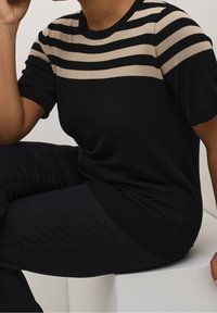 Mustabeige raidallinen lyhythihainen neulepusero, jossa pyöreä pääntie. Siinä on sileä neulospinta ja rento istuvuus.