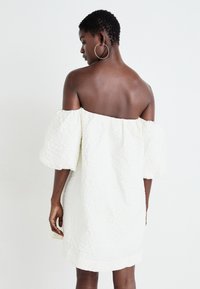 Biela off-the-shoulder šaty s textúrovanou látkou, krátkymi pufovanými rukávmi a voľným strihom, ktorý ukazuje jednoduchý a elegantný dizajn.
