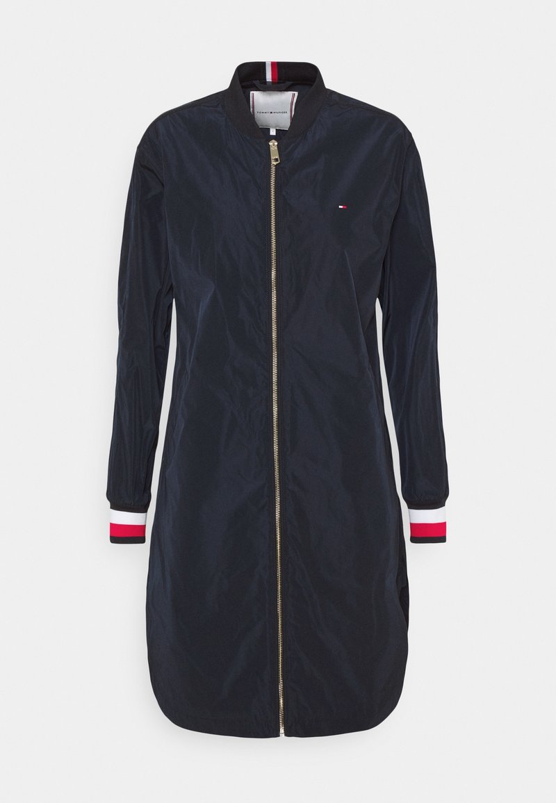 Veste bomber longue bleu marine avec fermeture éclair dorée à l'avant, col et poignets côtelés avec des rayures rouges, blanches et noires, petit logo poitrine.