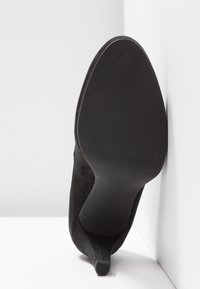 Chaussure à talon haut en suede noir montrant la semelle avec un motif en vagues, taille marquée comme 37, et un design de talon effilé.