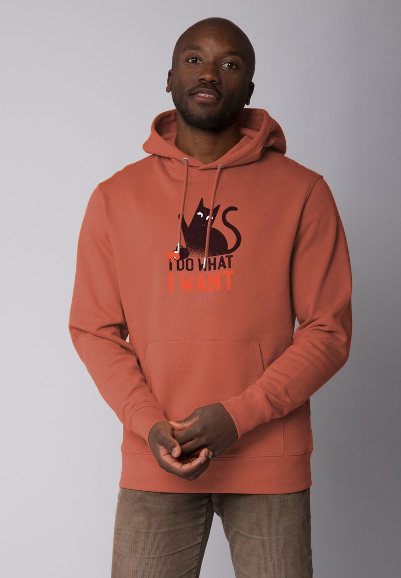 Haut à capuche couleur rouille avec poche kangourou et cordon de serrage, présentant un graphisme de chat noir et la phrase "JE FAIS CE QUE JE VEUX" en orange.