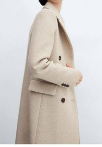 Beige uldblandingsfrakke med skræddersyet design, dobbeltknaplukning foran, brune knapper og sidelommer. Blød tekstur og struktureret silhuet.