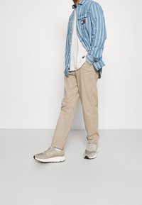 Lichtblauw gestreepte shirt, wit T-shirt, beige broek, grijs en witte sneakers. Casual outfit met zichtbare texturen en patronen.
