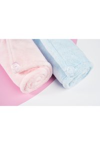 To rullede håndklær: ett mykt rosa og ett mykt blått. Hvert av dem har en knappdetalj. Teksturen ser fluffy og plysjaktig ut.