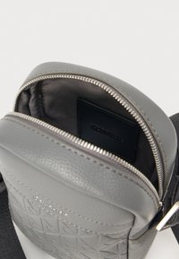 Borsa a spalla in pelle grigia con chiusura a zip, motivo texturizzato e interno liscio. Include un portacarte nero all'interno.