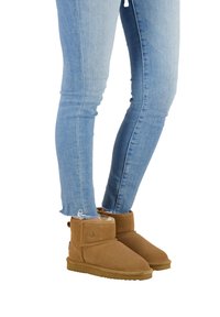 Brązowe zamszowe botki za kostkę z zagiętym mankietem, miękką podszewką i płaską gumową podeszwą, w połączeniu z jasnoniebieskimi skinny jeansami z postrzępionymi brzegami.