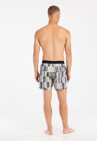 Bañadores de hombre con un patrón geométrico en tonos de azul y beige, con una cinturilla elástica negra y un bolsillo trasero.