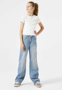 Lichtblauwe wijde jeans met een vervaagde afwerking, gecombineerd met een witte ribbeltrui met korte mouwen en grijze sneakers. Casual outfit ontwerp.