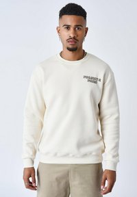 Sweatshirt crème avec des poignets et un ourlet côtelés, présentant un petit logo gris sur la poitrine. Tissu lisse, coupe décontractée, design minimaliste.