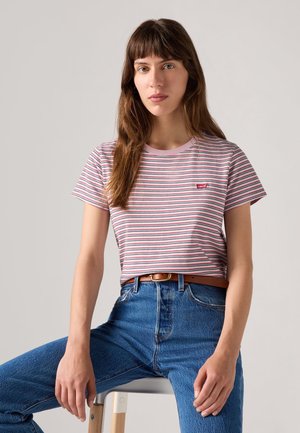 Camiseta de Rayas con líneas rosas, rojas y azules, de manga corta y cuello redondo. Presenta una pequeña etiqueta de logo roja en el lado izquierdo del pecho. Combinada con jeans de cintura alta azules.