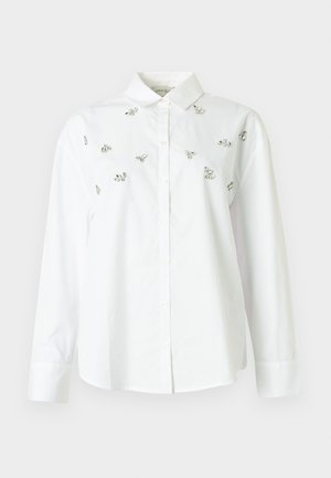 Chemise blanche boutonnée en coton, ornée de petits embellissements argentés dispersés. Manches longues et col classique.