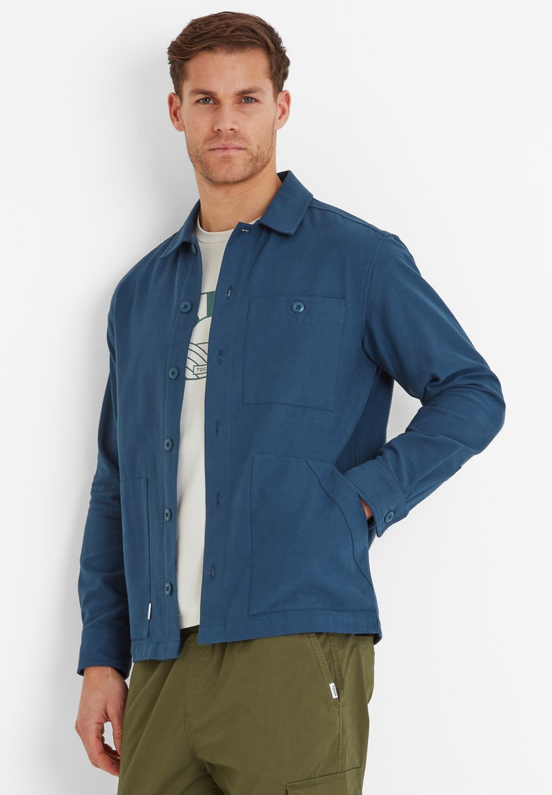 Blue button-up jacket made of soft fabric with a chest pocket, two lower pockets, and a collar. Worn over a light-colored t-shirt.