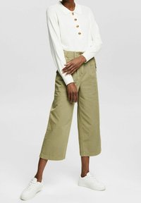 White long-sleeve collared top with wooden buttons paired with high-waisted olive green wide-leg trousers and white sneakers.