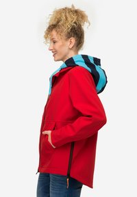 Giacca softshell rossa con cappuccio a strisce blu e navy, tasche laterali con zip e cordoncino regolabile. Texture liscia e vestibilità rilassata.