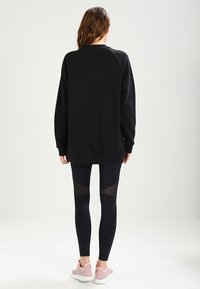 Svart överdimensionerad sweatshirt med raglanärmar, kombinerad med svarta leggings med nätpaneldetaljer och ljusrosa sneakers.